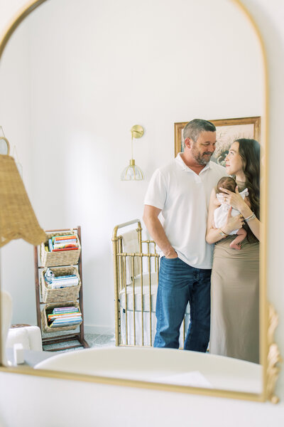 Mom-and-dad-cradling-baby-through-nursery-mirror-in-Austin