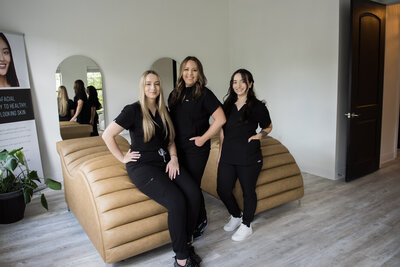 Three female estheticians in scrubs smiling