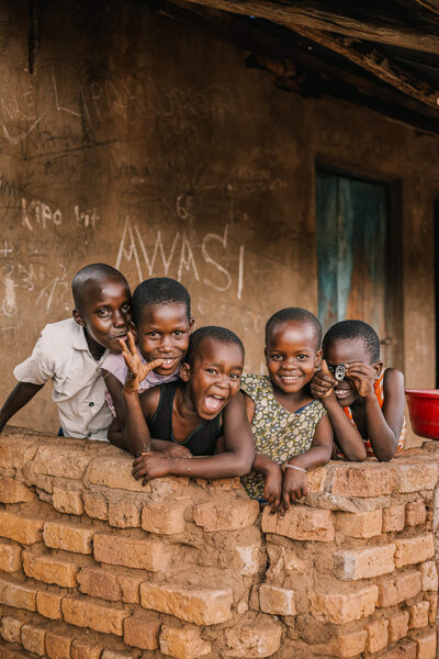 Children smiling looking over a brick wall