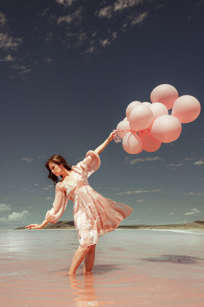 women holding balloons in right hand, blue skies, pink dress