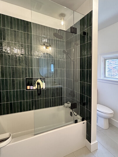 A bathtub with vertical emerald green tiling on the wall and black plumbing fixtures