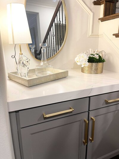 An elegant entrance for a luxury home in Frisco, featuring a wooden table with a lamp and glass decoration, along with a stylish mirror on the wall.