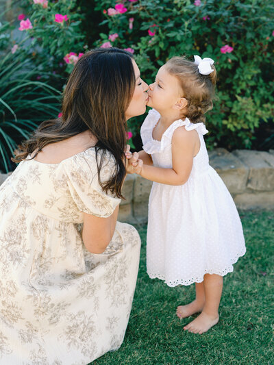 garden portrait of mom and toddler girl sharing a sweet kiss