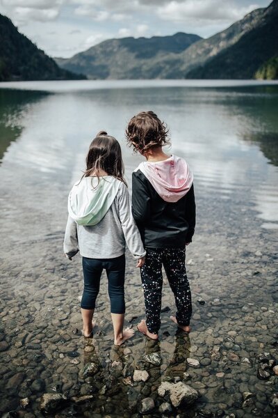 the backs of two kids standing side by side in a lake