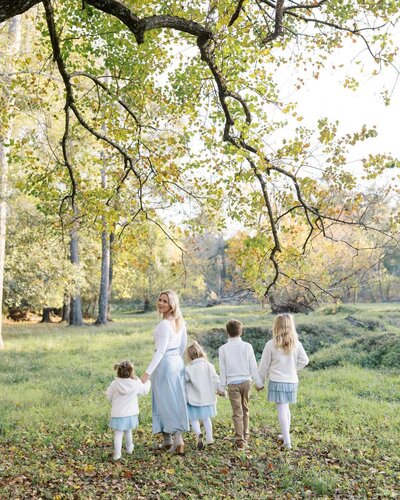 Stephanie Houseal and her children walk through a sunlit field, capturing the beauty of motherhood. A glimpse into Moments in Light Photography.