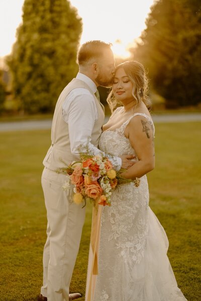 Bride and groom embracing surrounded by greenery during sunset