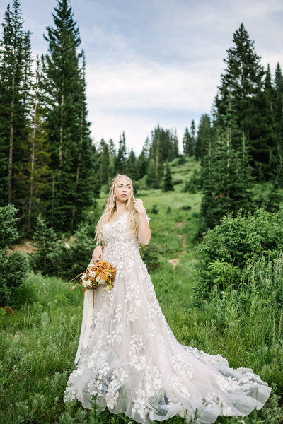 bride standing in a field in her wedding dress while holding her bridal bouquet