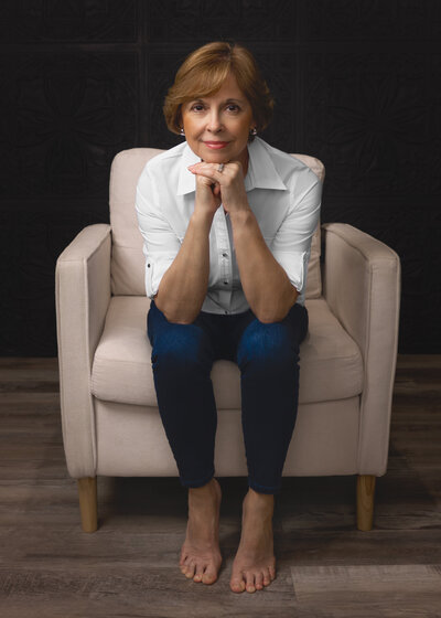 older lady sitting in white chair with hands under chin