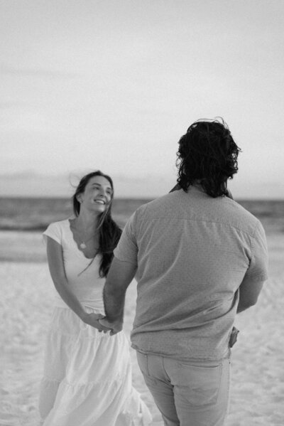 a black and white photo of a couple swinging around in a circle in the sand at Grayton Beach, Florida.