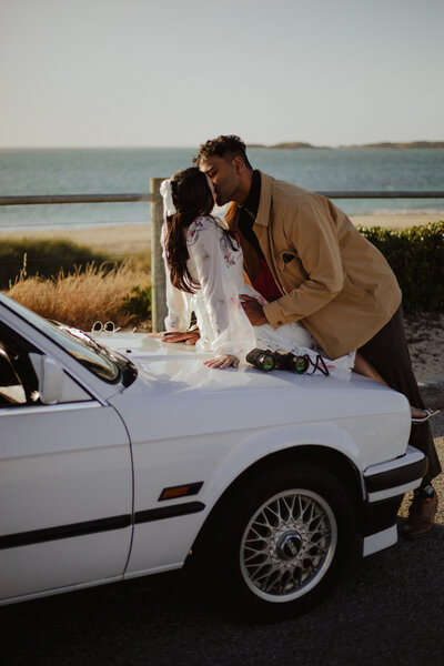 Couple sitting on bench at the beach, her legs draped over his & looking at each other