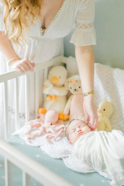 Sleeping baby nestled in her crib, peacefully resting. Mom leans over the crib, gazing lovingly at her little one with a tender, serene expression, creating a quiet, intimate moment in the nursery