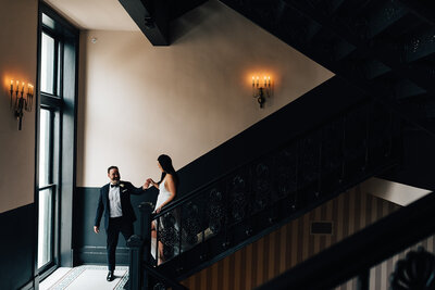 Groom helps his bride walk down the stairs by holding her hand by Casey McMurray Photography