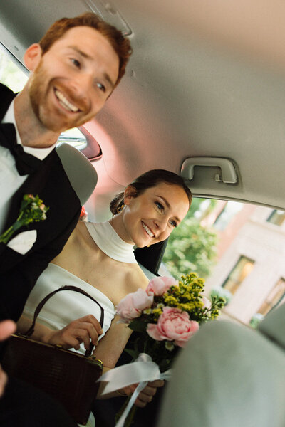 smiling and happy bride and groom in car after eloping in the city 