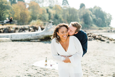 interracial couple embraces on beach for engagement photos