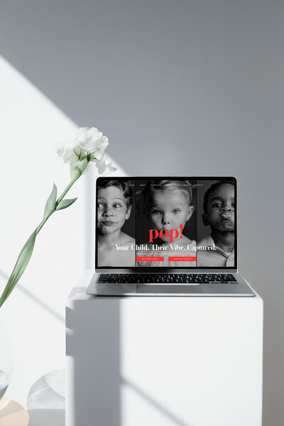 Laptop on a white table beside a white flower, showcasing a clean and modern design for a photographer's website.