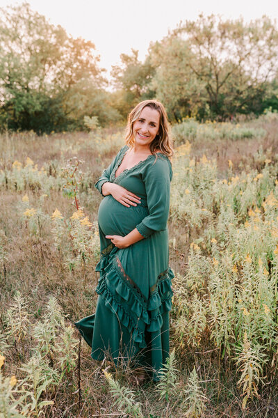 woman in green dress hold her belly in a beautiful field as she wears a Baltic Born dress