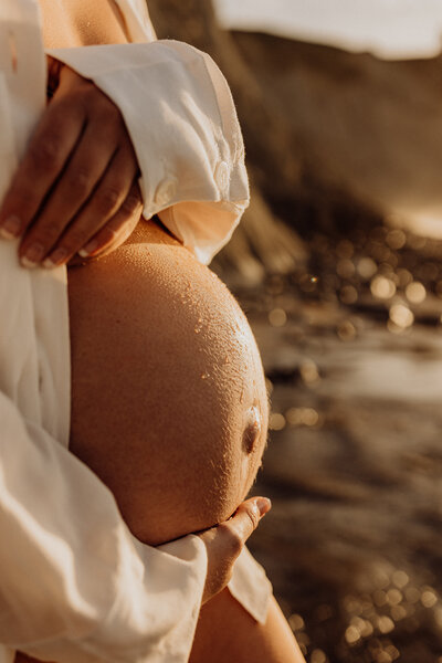 A pregnant woman holding her belly during a sunset photoshoot in christchurch with lucy jane
