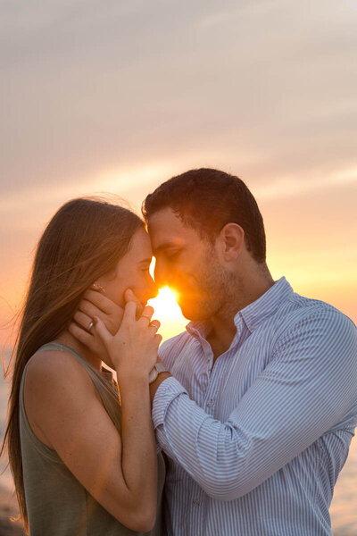 Couple rests heads together as sun sets between them