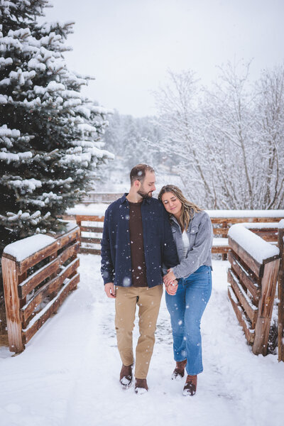 An engaged couple walking down a snowy boardwalk holding hands