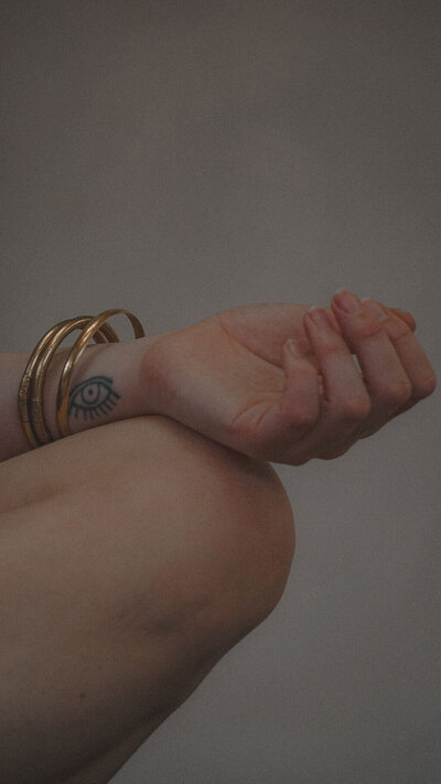 Close-up of a hand with a tattooed eye and gold bracelets, symbolizing sacred focus and spiritual intention.
