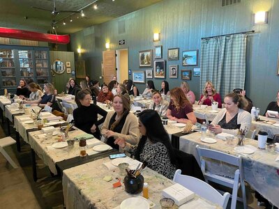 group of women sitting at tables with art supplies