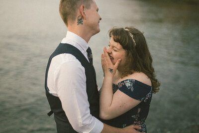 bride and groom laugh on the lake shore