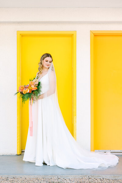 bride against bright yellow door with bouquet
