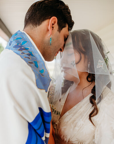 A couple stands close under a translucent veil