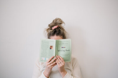 Woman with a messy bun holding up a Writing Tools book in front of her face