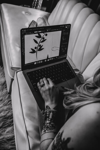 A black and white photo of a woman looking at a laptop. The screen shows a digital illustration of an olive branch.