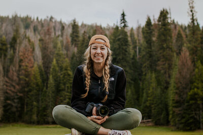 Noël Brower sits on a rock in meadow with camera on her lap