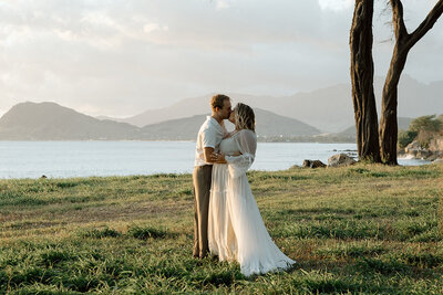 bride and groom snuggle in a field at sunset