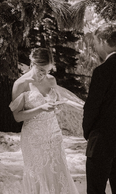 A bride and groom share vow out of vow books in a snowy setting with pine trees in the background.