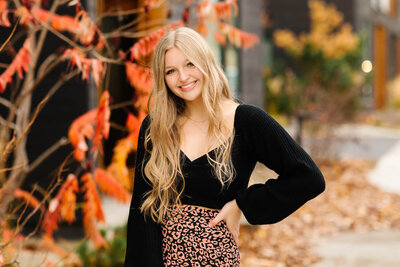 blonde high school senior in leopard print skirt with fall leaves behind her