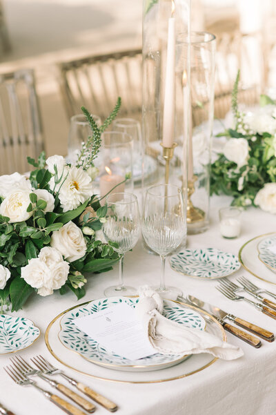 Wedding reception table close up with a teal patterned scalloped plate, wooden cutlery, and white flowers