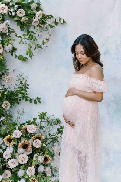 Richmond maternity photographer | Light and airy photo of a pregnant mother in a pink lace dress standing in front of a water color backdrop and floral arch by Jacqueline Aimee Portraits