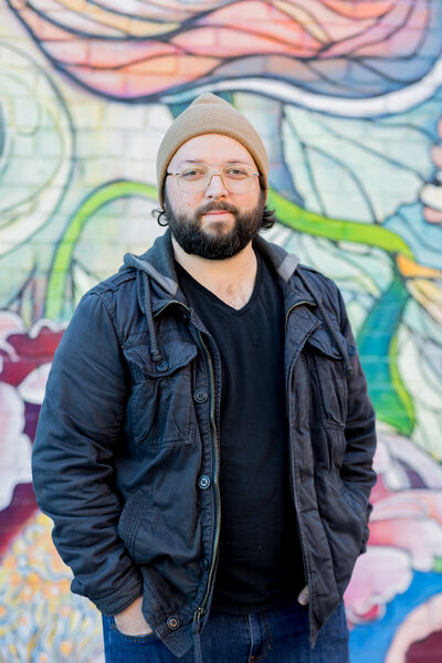 Professional branding portrait of a man wearing a beanie and glasses, standing confidently against a vibrant mural in Columbia, SC. His casual yet polished look makes for an approachable and modern business headshot perfect for personal branding.