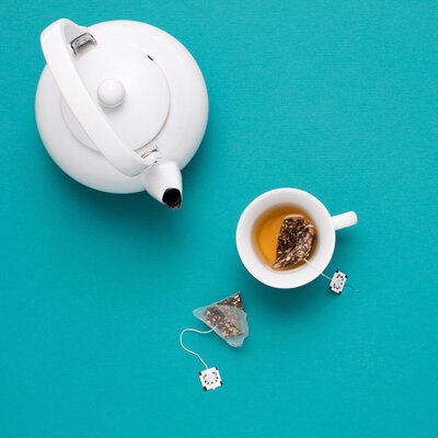 A tea kettle, a cup of tea, and a tea sachet beside the tea cup