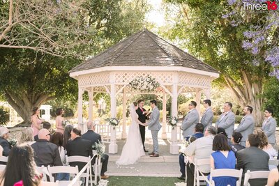 Bride and Groom hold hands under a gazebo during their wedding ceremony at the Heritage Museum of Orange County in Santa Ana