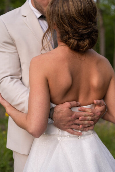 Groom's hands clasped around the bride's back to hug