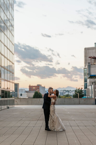 A newlywed couple kissing on the rooftop of a high rise