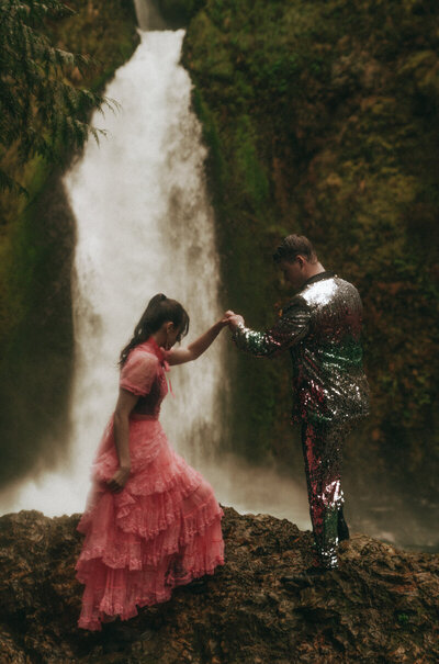 Eloping couple holding hands with a scenic waterfall in the background.