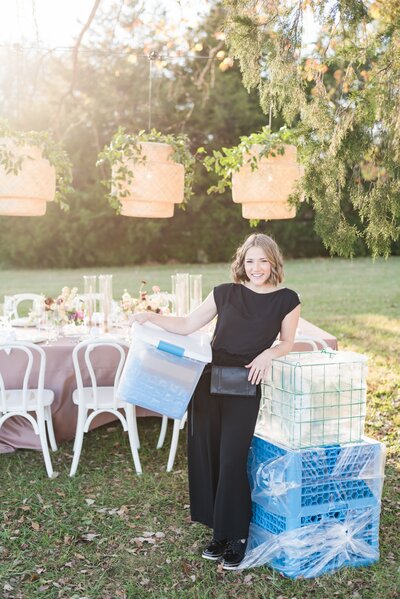 Branding photo for Nashville wedding planner wearing all black and standing next with blue crates and bins with tableware