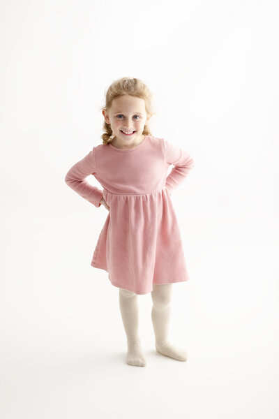 This milestone portrait of a girl in a soft pink dress exudes confidence and joy, all captured in a clean and bright studio setting.