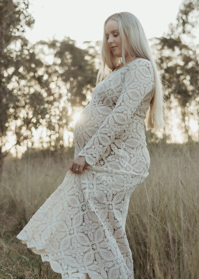 Pregnant mama in strapless green dress cradling her belly while sitting in a grassy field with the sun glowing on her