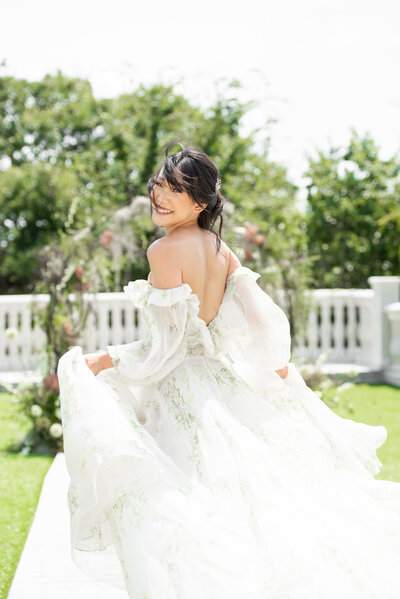 Bride in flowing wedding dress runs across terrace and smiles