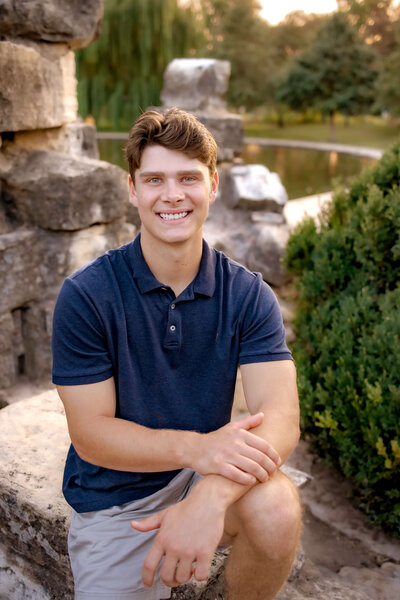 a young man is sitting on the ledge of a stone structure inside Tower Grove Park in St. Louis for his Senior portraits.