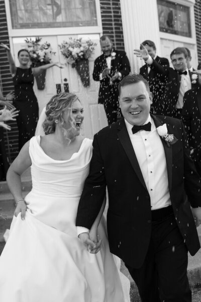 Bride and groom smile as they walk under rice being thrown on the way out from their ceremony