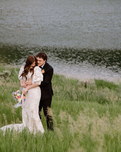 groom hugging bride from behind by lake