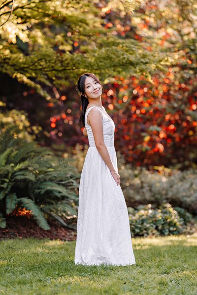 Senior portrait of a girl posing confidently against a backdrop of vivid fall foliage in warm autumn tones.